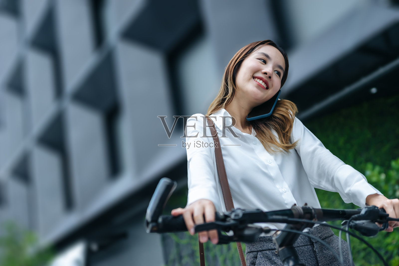 年轻的亚洲女商人戴着头盔，骑着自行车站在城市街道上看手机。照片摄影图片