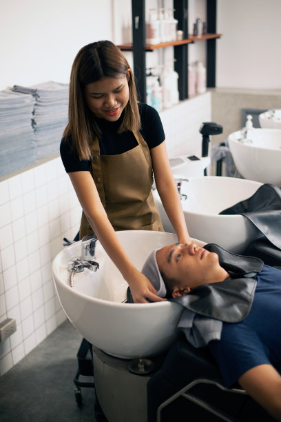 理发师在理发店里为顾客洗头,一名男子躺在椅子上,穿着长袍,专业地