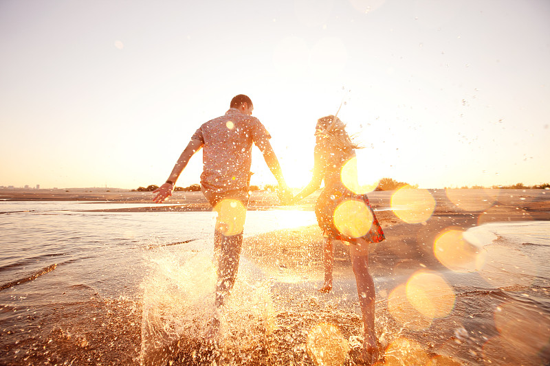 一对快乐的夫妇在阳光照耀的海滩上冲过海浪图片下载
